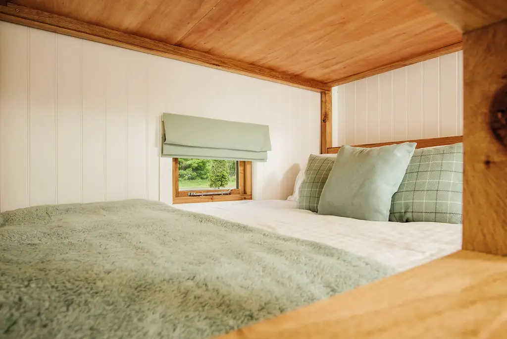 Double bed with green throw and cushions in shepherd's hut