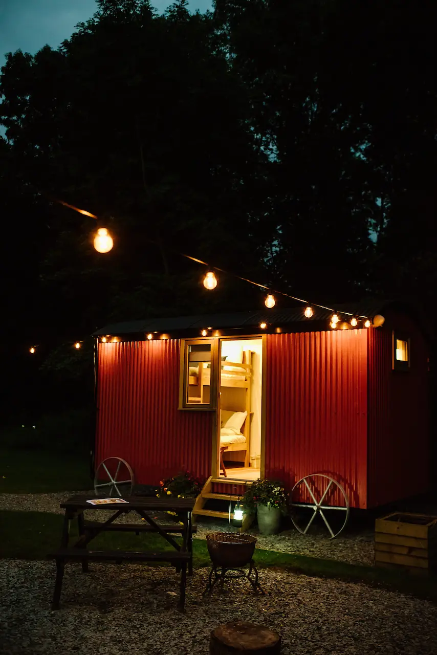 Single red shepherd's hut at night with light on inside and festoon lights