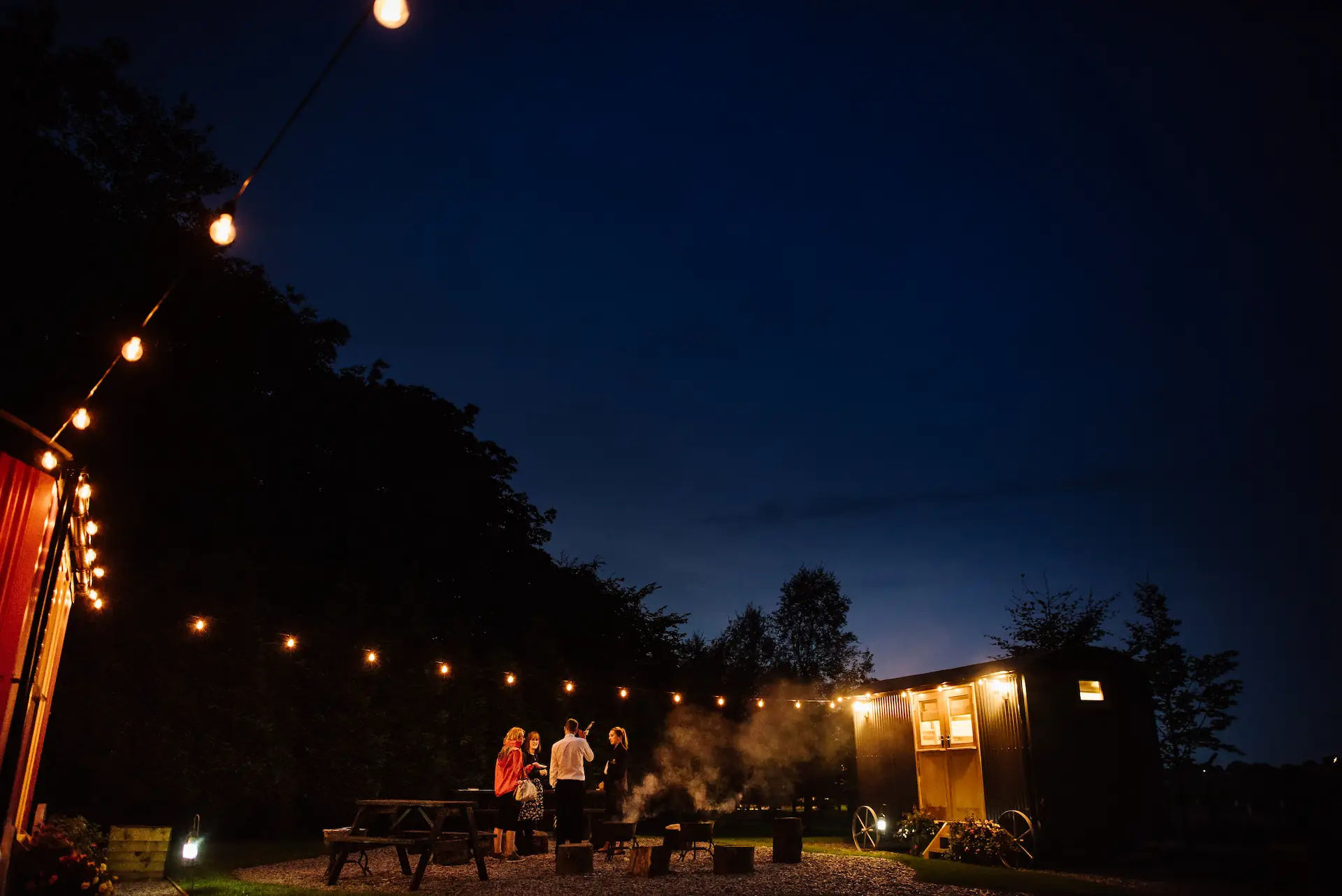 Shepherd's huts at night with festoon lights and people stood outside