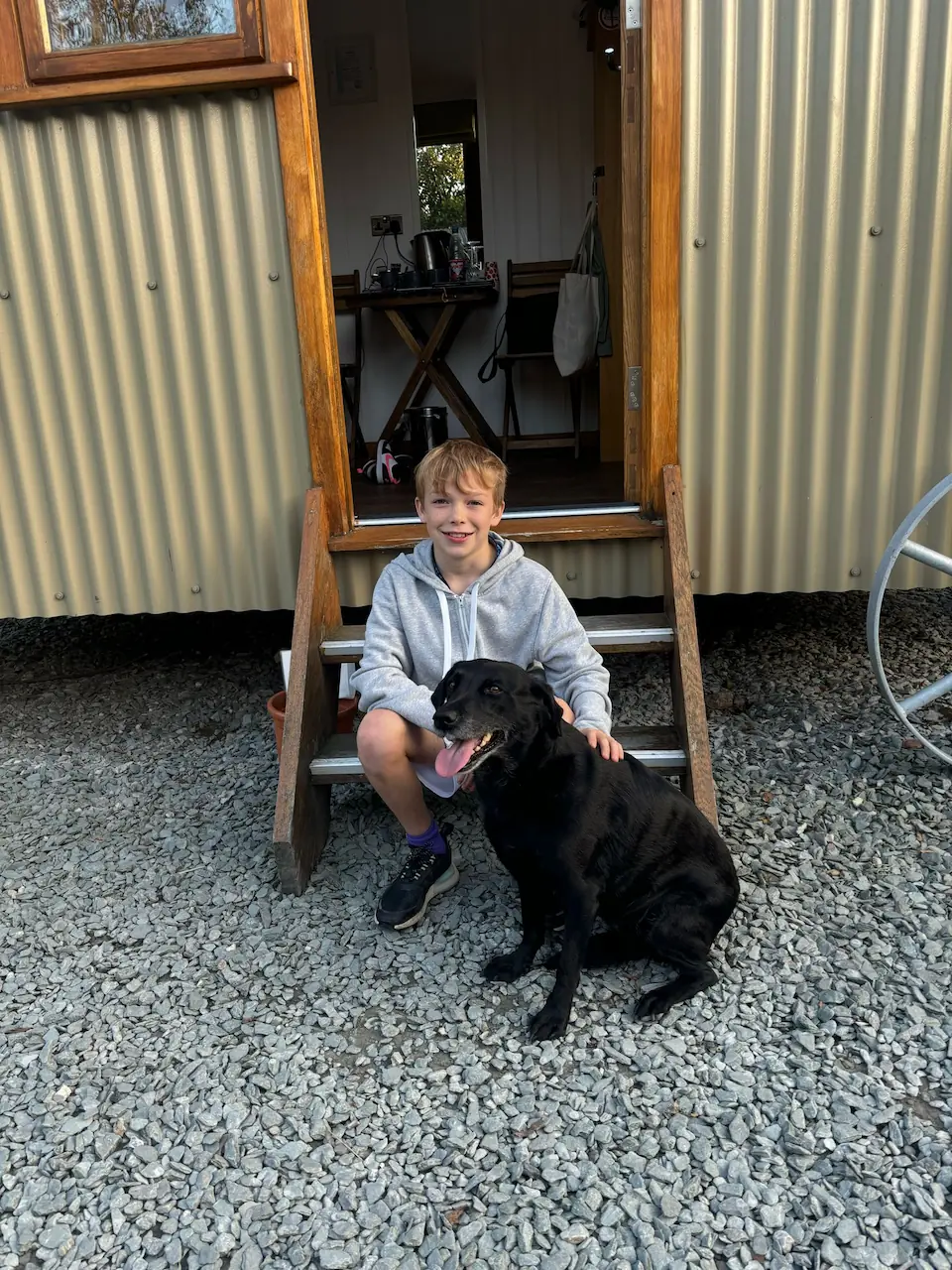 Child sat on the steps of a shepherd's hut with a dog