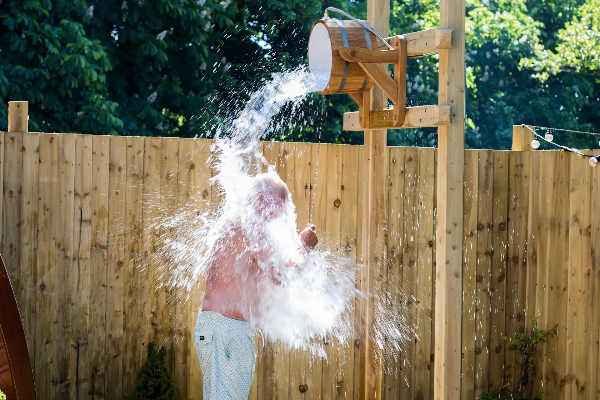 Man stood beneath cold water bucket shower with water pouring out