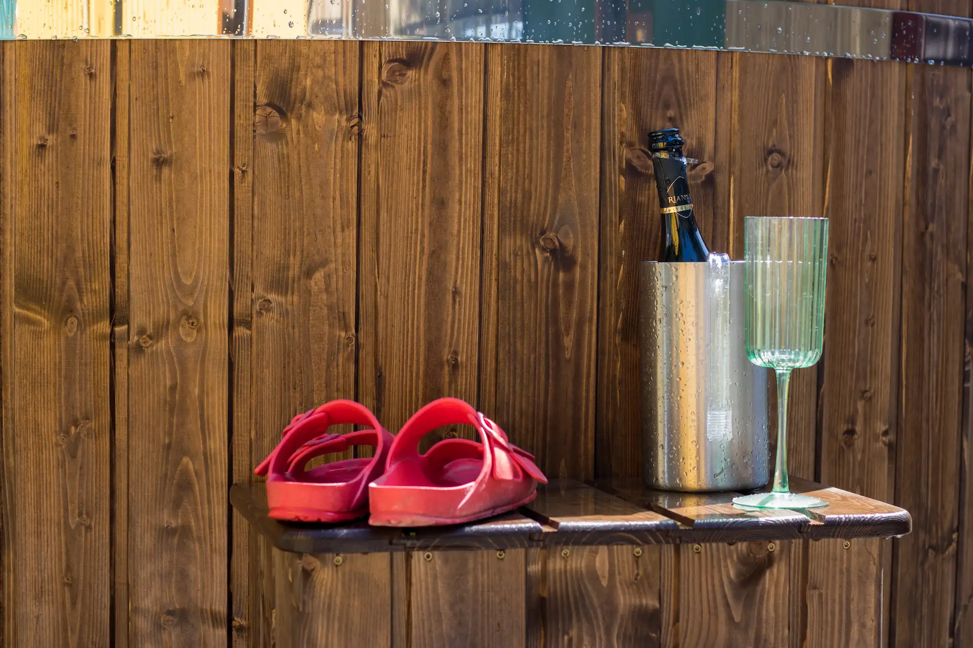 Sandals, wine bottle and glass on a table with fence in background