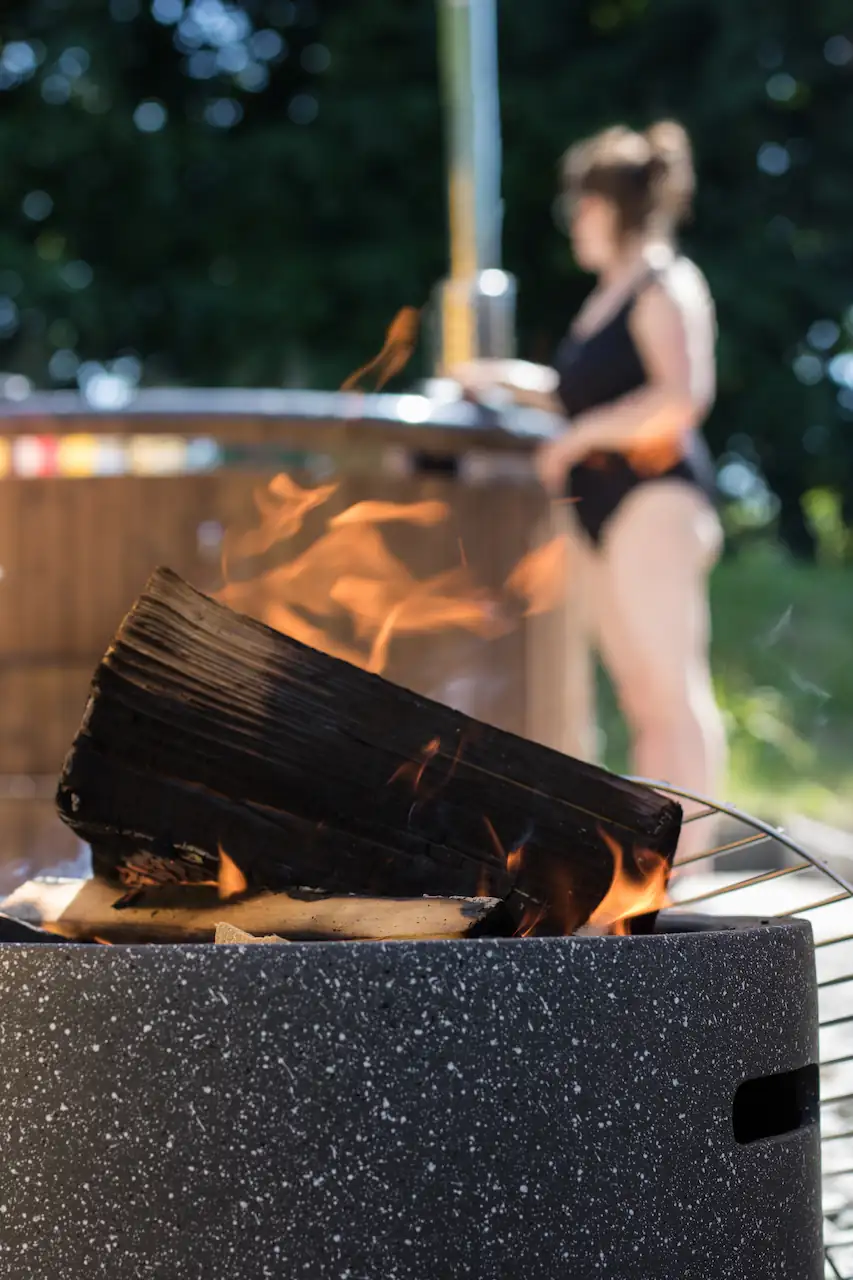Fire pit in the foreground with woman in swimming costume stood by a hot tub