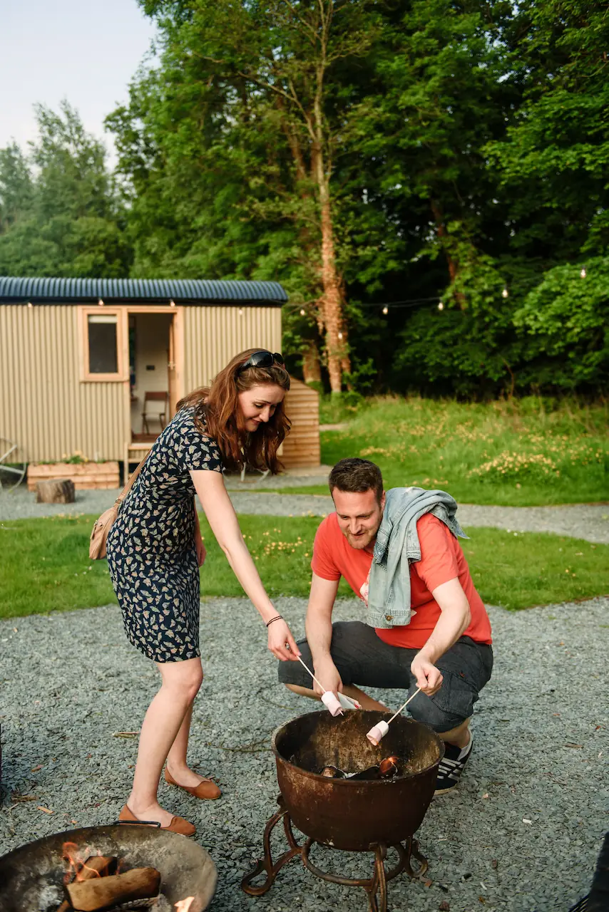 Couple toasting marshmallows at a firepit outside a shepherds hut